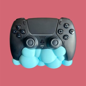May include: A black PlayStation 5 controller with light blue cloud-like detailing. The controller has the standard button layout, including a directional pad, action buttons, and analogue sticks. The PlayStation logo is centered.