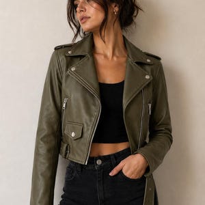 May include: Olive green leather jacket with a classic biker style, featuring a notched collar, asymmetrical zip closure, and multiple pockets. The jacket is paired with a black top and black jeans.