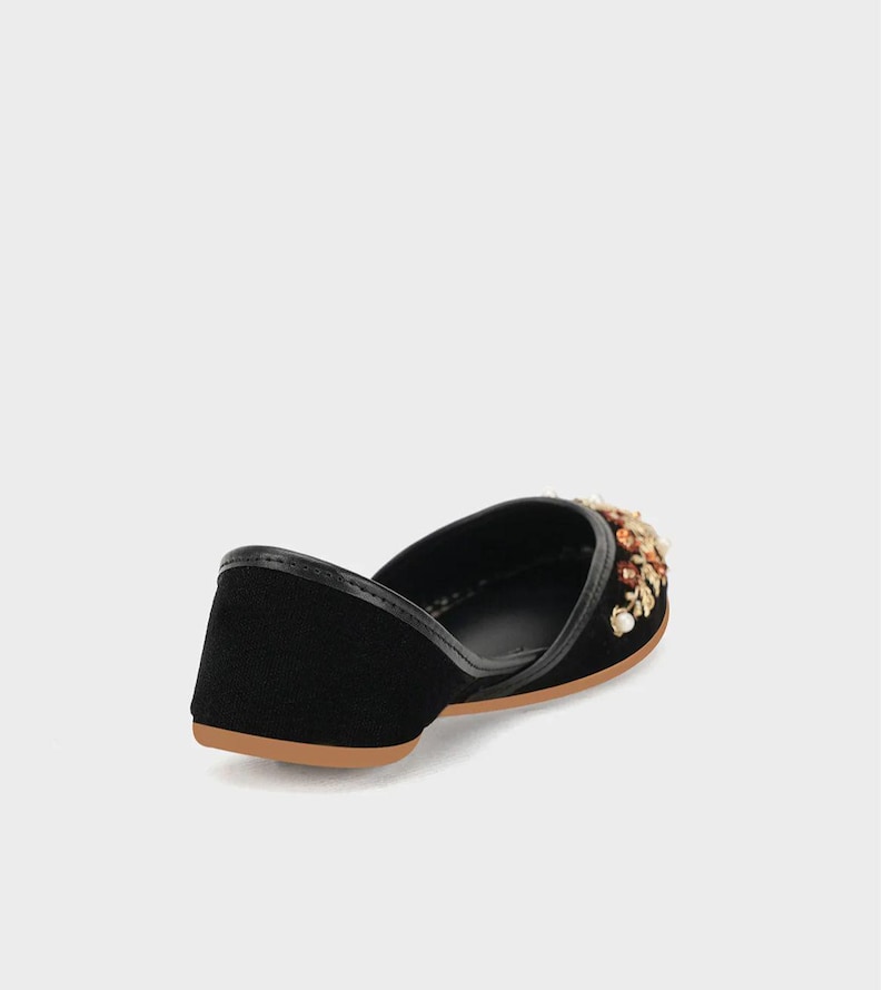 May include: Black velvet flat shoe with a decorative floral embellishment in shades of gold, brown, and cream. The shoe has a leather trim and a tan sole. This elegant shoe is perfect for special occasions.