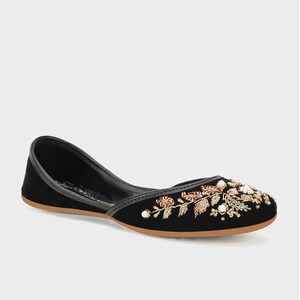 May include: Black velvet flat shoe with floral embroidery. The shoe features a rounded toe and a low heel. The floral design includes gold, red, and white accents. The sole is a light brown color.
