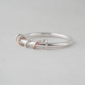 Könnte beinhalten: Ein silberner Ring mit mehreren kleineren Ringen aus Silber und Roségold, die um ihn herumgewickelt sind.