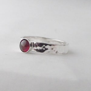 May include: A silver ring with a hammered texture and a small, round, red gemstone.