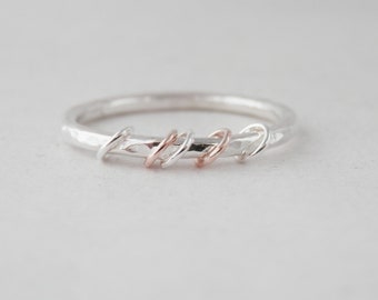 Op de afbeelding: Een zilveren ring met een gehammerde textuur en vijf kleine, in elkaar verweven ringen, waarvan er twee van roségoud zijn.