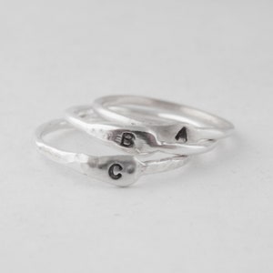 May include: Three silver rings stacked on top of each other. The rings are textured and have the letters A, B, and C engraved on them.