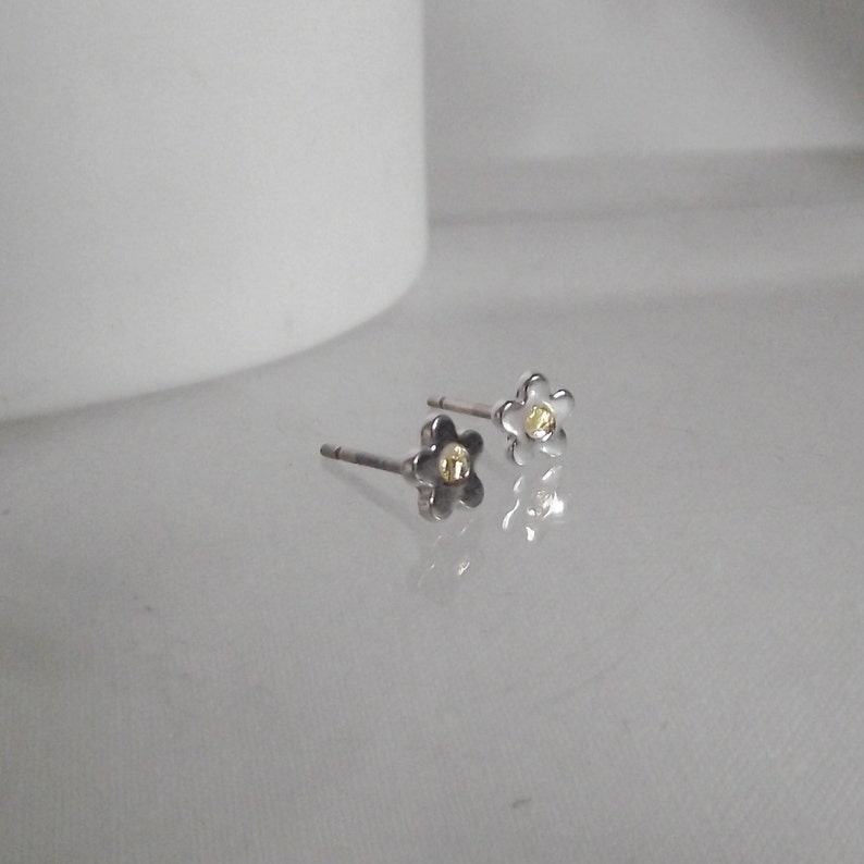 May include: A pair of silver flower stud earrings with a gold center. The earrings are small and delicate.