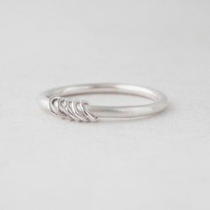 May include: A silver ring with a series of small, connected circles on one side.