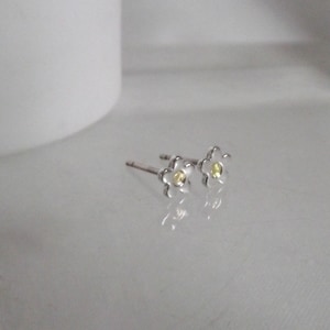 May include: A pair of silver flower stud earrings with a yellow center stone.