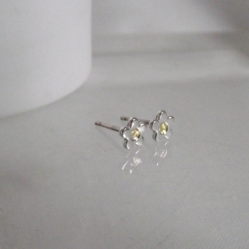 May include: A pair of silver flower stud earrings with a yellow center stone.