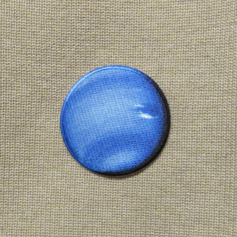 May include: A round, blue patch with a textured surface and a black border. The patch has a watercolor effect, with lighter blue areas. The background is a tan, woven fabric.