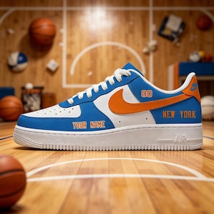 May include: A blue and white sneaker featuring an orange swoosh, white laces, and a white sole. The side displays the text "YOUR NAME" and "NEW YORK" in orange lettering, with the number "00" printed near the collar and "AIR" on the midsole.
