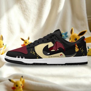 May include: Black, red, and cream-colored sneaker featuring a Charizard design. The shoe has a white sole and a black upper with a cream-colored swoosh. The design includes a Charizard graphic and the text "NO.006 CHARIZARD".