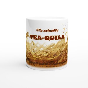 May include: White ceramic mug with the text "It's actually TEA-QUILA" in brown lettering. The mug features a brown liquid splash design, suggesting a beverage. The mug is a standard size for hot drinks.