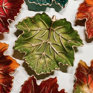 May include: A collection of leaf-shaped dishes featuring metallic gold veins and glossy enamel finishes in shades of red, orange, and green. Each dish mimics the organic form of a foliage leaf with scalloped edges and a central stem detail.