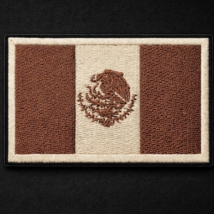 Op de afbeelding: Geborduurde patch met de Mexicaanse vlag. Het ontwerp bevat verticale strepen in bruin en gebroken wit, met het Mexicaanse wapen in het midden. De patch heeft een zwarte rand en is geplaatst tegen een zwarte achtergrond.