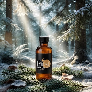 May include: An amber glass bottle with a black cap and a black label featuring the white text First impression SCENTS. The bottle is surrounded by green pine needles on a snowy ground, with sunlight filtering through the trees in the background.