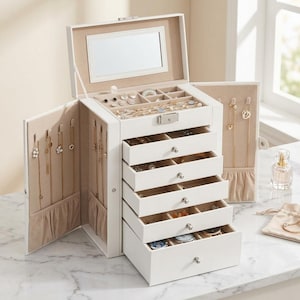 May include: A white jewelry armoire with multiple drawers and compartments. The armoire has a built-in mirror and is open, displaying various necklaces, earrings, and other jewelry. The drawers are filled with rings, bracelets, and watches. The armoire is on a marble surface.