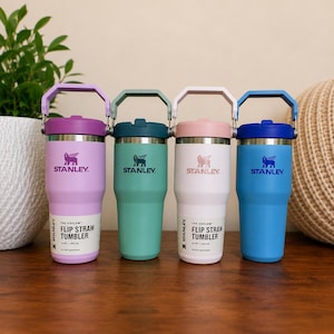 May include: Four Stanley Flip Straw Tumblers in pastel colors: lavender, teal, pink, and blue. Each tumbler has a matching handle and lid, with the Stanley logo and "Flip Straw Tumbler" text visible. The tumblers are 14 oz / 400 ml.
