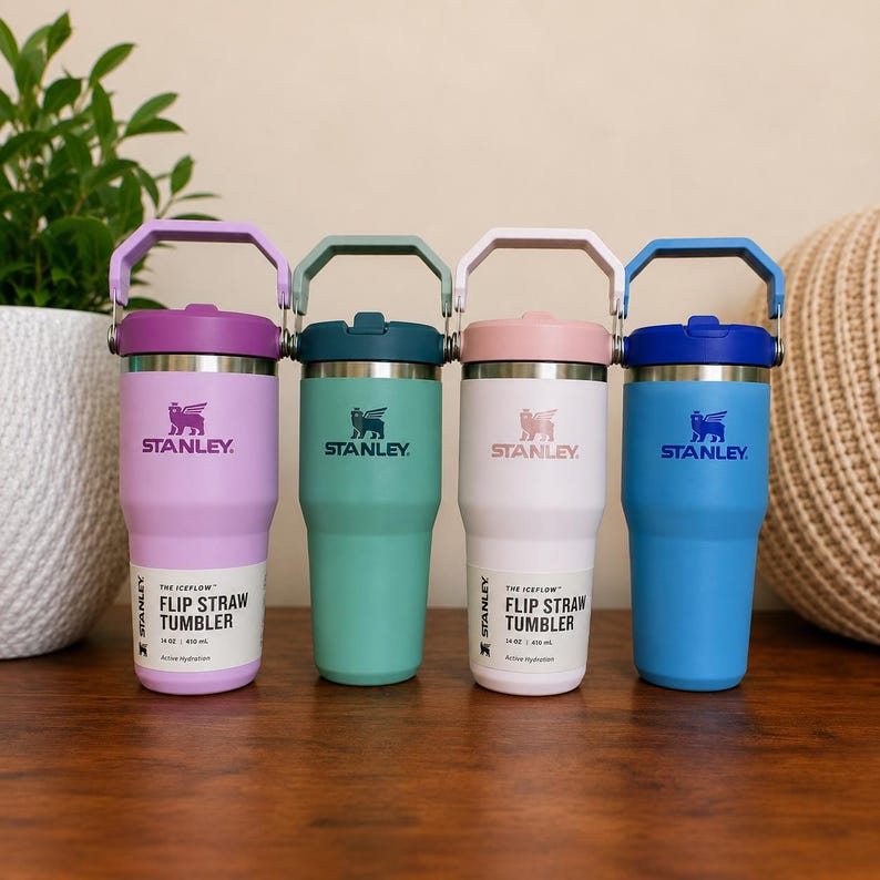 May include: Four Stanley Flip Straw Tumblers in pastel colors: lavender, teal, pink, and blue. Each tumbler has a matching handle and lid, with the Stanley logo and "Flip Straw Tumbler" text visible. The tumblers are 14 oz / 400 ml.