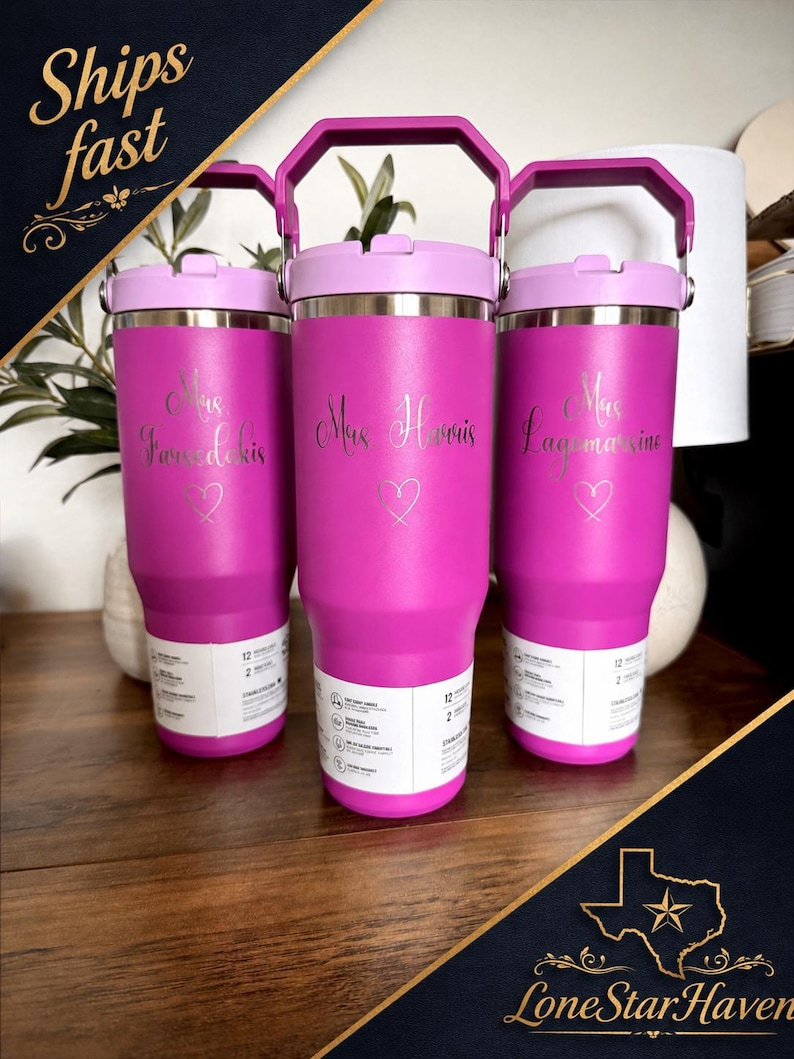 K&ouml;nnte beinhalten: Drei leuchtend pinke Edelstahlbecher mit violetten Deckeln und Griffen. Jeder Becher ist mit einem in Schreibschrift gravierten Namen &uuml;ber einem kleinen Herzumriss versehen. Ein wei&szlig;es Produktetikett ist um den unteren Teil gewickelt.