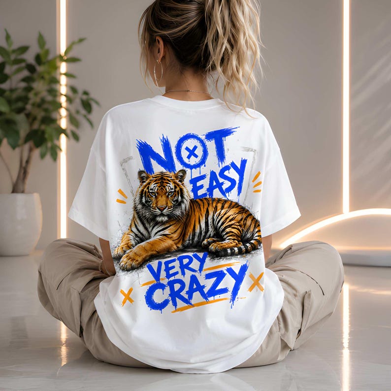 May include: White t-shirt with a tiger graphic and the text "NOT EASY VERY CRAZY" in blue and orange. The tiger is orange and black. The shirt is a casual style.