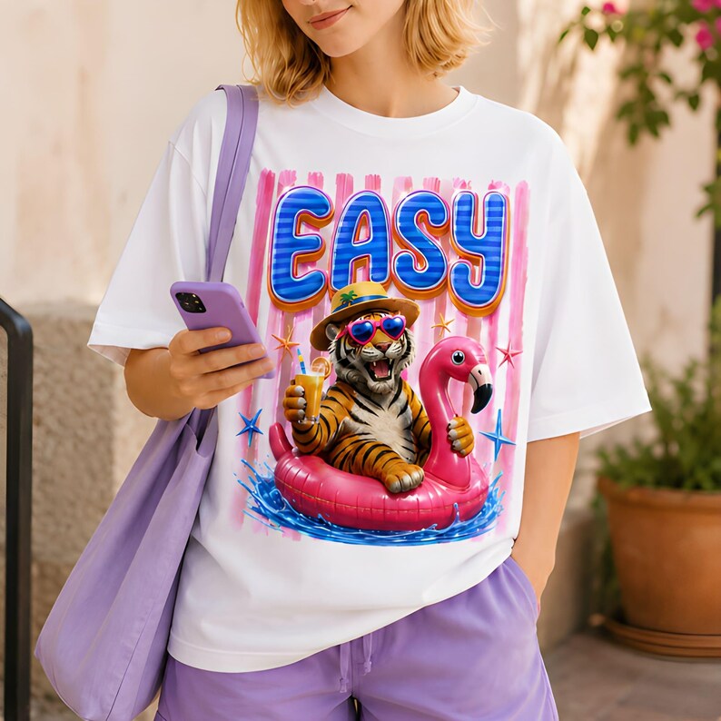 May include: White t-shirt with the word "EASY" in blue and pink. The graphic features a tiger wearing sunglasses and a hat, floating on a pink flamingo floatie and holding a drink. The shirt is paired with purple shorts.