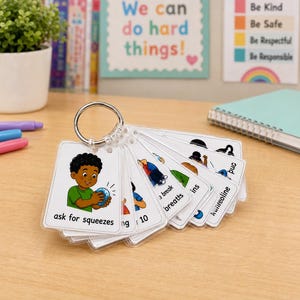 May include: A set of laminated communication cards on a metal ring, each featuring a cartoon illustration of a person performing an action and corresponding text, such as ask for squeezes, take a break, take breaths, and use trampoline.