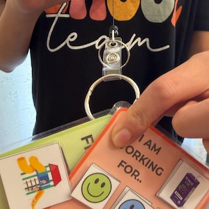 May include: A retractable badge reel attached to a metal ring holding a laminated visual communication board. The board features the text I AM WORKING FOR, a juice box graphic, and five colorful smiley face icons in green, blue, pink, orange, and yellow.