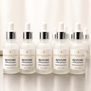 Puede incluir: Cinco frascos cuentagotas de vidrio esmerilado de Peptalume Restore Concentrate Peptide Architectural Serum. Cada frasco tiene una etiqueta blanca con texto dorado, un cuello plateado y una tapa cuentagotas blanca, etiquetado como Net 1 fl oz / 30 ml.
