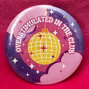 May include: A pink and purple button with a disco ball and the text "Overstimulated in the club".