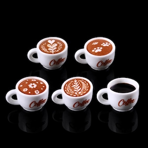 May include: A set of three ceramic mugs with a speckled, cream-colored glaze. Each mug features a different hand-painted design: a blue and green leaf, a yellow and orange flower, and a red and pink berry. The mugs have a simple, rounded shape.