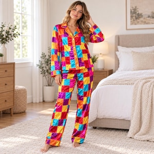 May include: A two-piece pajama set featuring a long-sleeved button-down shirt and matching straight-leg pants. The garment is made of a shiny, satin-like fabric with a vibrant, multi-colored patchwork pattern in shades of red, orange, blue, and purple.