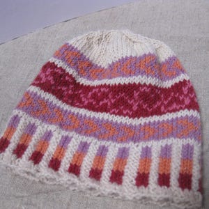 Puede incluir: Un gorro de punto crema, con bandas de patrones geom&eacute;tricos rojos, rosas, naranjas y morados. El gorro presenta un borde acanalado y un aspecto suave, adecuado para el clima fr&iacute;o.