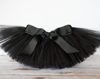 May include: A black tulle tutu with a large black satin bow. The tutu is made of soft, delicate tulle and is perfect for a special occasion.