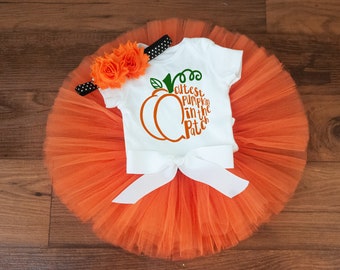 May include: Orange tulle tutu skirt with a white shirt that says "Cutest Pumpkin in the Patch" and a flower headband.