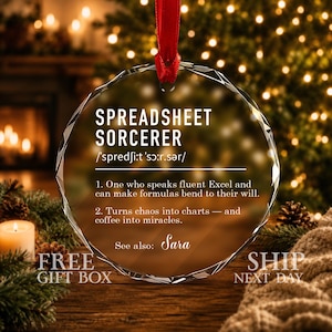 May include: A circular clear glass ornament with a faceted edge, suspended by a red ribbon. The text reads: SPREADSHEET SORCERER, phonetic spelling, and two definitions regarding Excel formulas and charts, with the name Sara at the bottom.