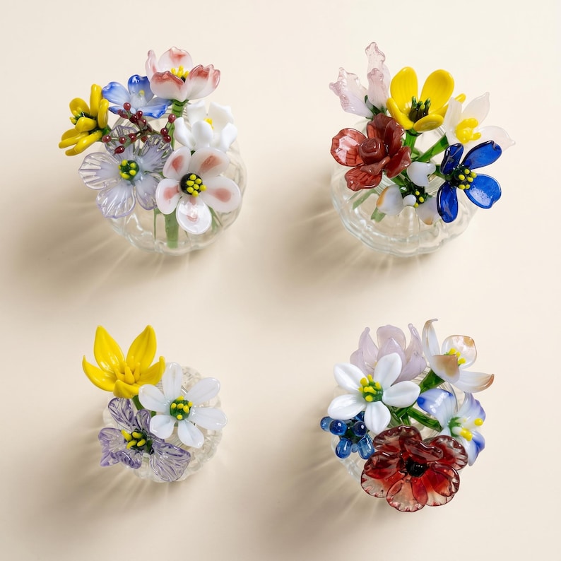 May include: Four miniature glass flower arrangements. Each features a collection of colourful glass flowers, including yellow, white, blue, and red. The flowers are arranged in small, clear glass vases, creating a delicate and artistic display.