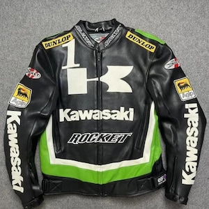 Puede incluir: Chaqueta de moto Kawasaki negra con detalles blancos y verdes. Presenta el logotipo de Kawasaki, la palabra "ROCKET" y logotipos de patrocinadores. La chaqueta tiene cierre de cremallera y es de cuero.