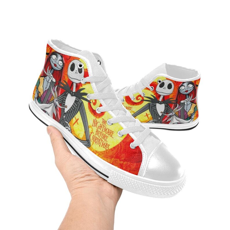 May include: High-top canvas sneakers featuring a vibrant yellow and orange background with a graphic print of Jack Skellington, Sally, and Zero from The Nightmare Before Christmas. The shoes have white laces, white rubber toe caps, and white soles.