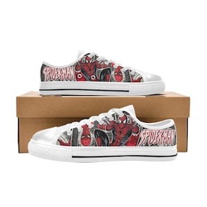 May include: Low-top sneakers featuring a white rubber toe cap, white laces, and a graphic print of the comic book character Spider-Man in red and black. The side panels display the text Spider-Man in a stylized font against a comic book background.