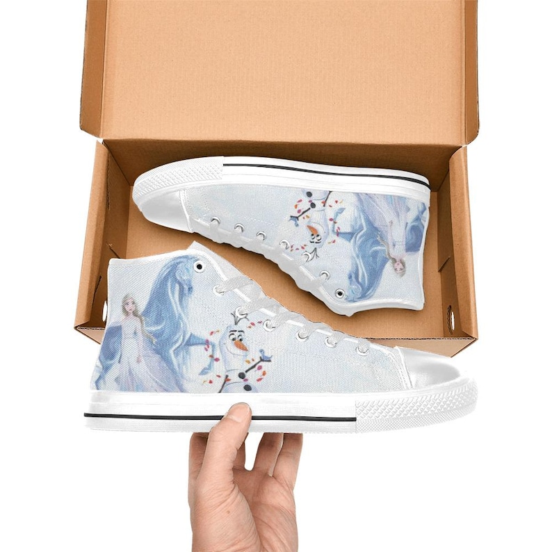 Pu&ograve; includere: Un paio di scarpe alte in tela bianca con una stampa grafica raffigurante un personaggio biondo con un abito lungo, un cavallo blu e un pupazzo di neve. Le scarpe presentano lacci bianchi, punte in gomma bianca e suole in gomma bianca con bordo nero.