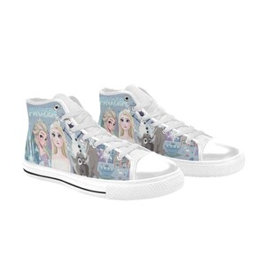 Pode incluir: Um par de t&eacute;nis de cano alto brancos com uma impress&atilde;o gr&aacute;fica em azul claro e roxo de personagens do filme Frozen, incluindo Elsa, Anna e Olaf. Os sapatos t&ecirc;m atacadores brancos, biqueiras de borracha branca e solas de borracha branca.