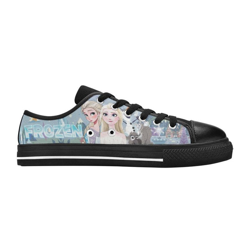 May include: A low-top sneaker with a black rubber sole, black laces, and a black toe cap. The side panel features a light blue graphic print of the characters Elsa and Anna from Frozen, along with the text Frozen, a snowman, and a reindeer.