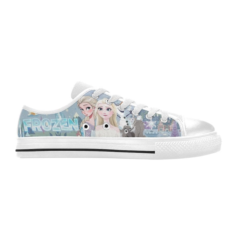 May include: A low-top canvas sneaker featuring a light blue graphic print of characters from the movie Frozen, including Elsa and Anna, with the text FROZEN visible on the side. The shoe has white laces, a white rubber toe cap, and a white sole.