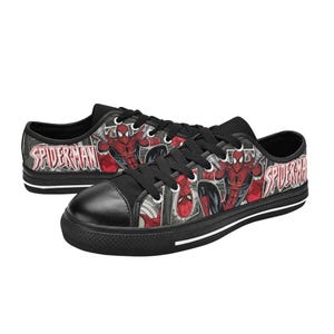 May include: Low-top sneakers featuring a black canvas upper with a red and black Spider-Man comic book graphic print. The shoes include black laces, black rubber toe caps, and black soles with white stripes. The text Spider-Man is printed on the side.