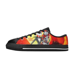 May include: A low-top trainer with a black rubber sole and black laces. The canvas upper features a vibrant orange and yellow background with a graphic print of Jack Skellington, Sally, and Zero, including the text The Nightmare Before Christmas.