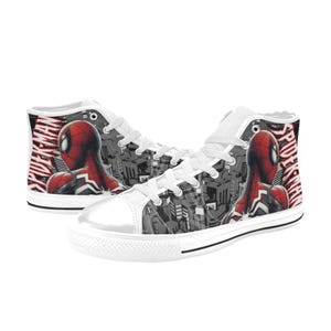 May include: White high-top sneakers featuring a Spider-Man design. The shoes have a red and black Spider-Man graphic on the sides, with the words "Spider-Man" in red. The background is a grayscale cityscape.