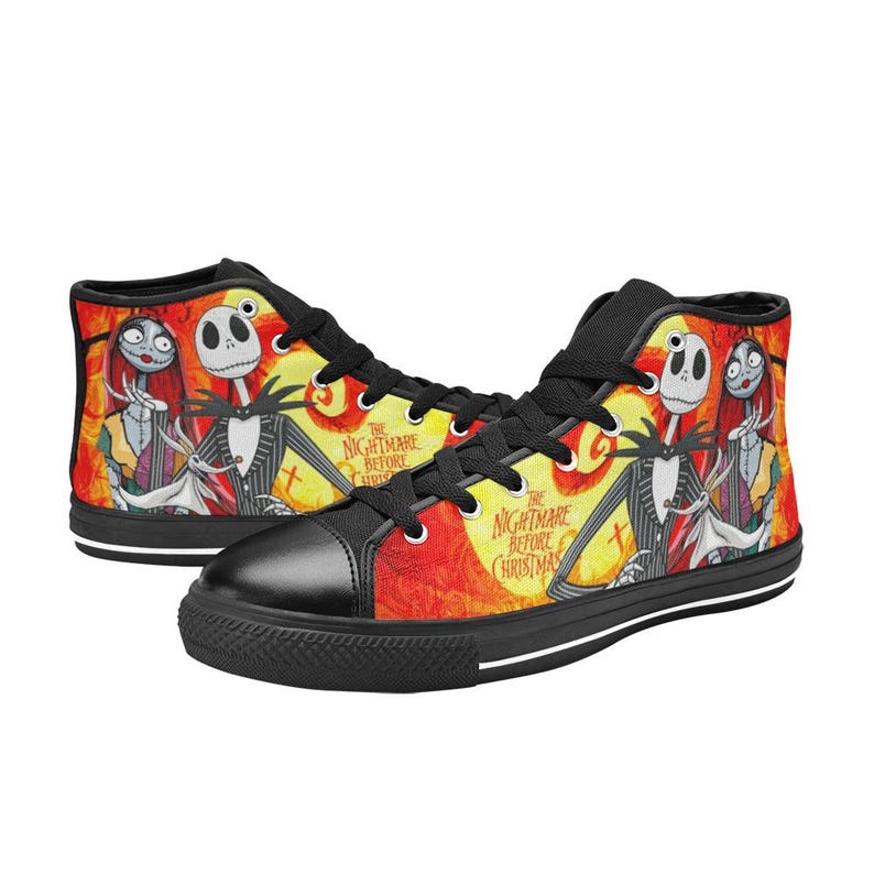 May include: High-top sneakers featuring a vibrant orange and yellow background with a graphic print of Jack Skellington, Sally, and Zero from The Nightmare Before Christmas. The shoes have black laces, black toe caps, and black soles with white stripes.