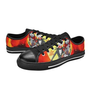 May include: Low-top trainers featuring a black toe cap, black laces, and a vibrant red and yellow graphic print of Jack Skellington, Sally, and Zero from The Nightmare Before Christmas. The shoes have a black sole with white trim detailing.