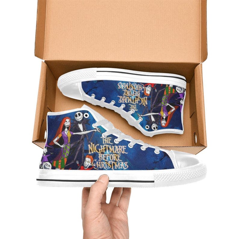 May include: High-top canvas sneakers featuring a blue background with The Nightmare Before Christmas characters and logo text. The shoes have white rubber toe caps, white laces, and white soles, displayed inside an open cardboard box.