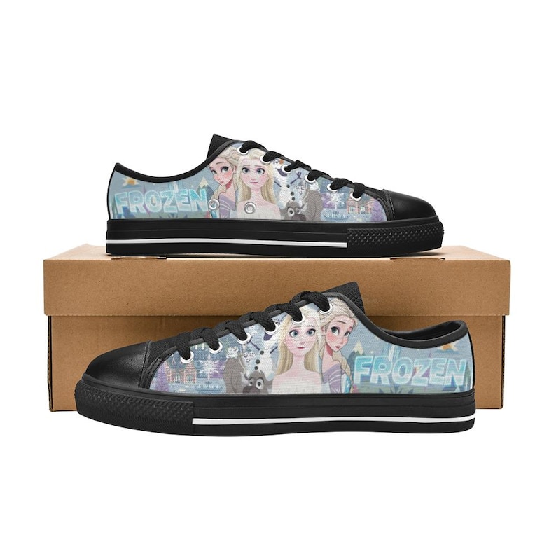 May include: Low-top canvas sneakers featuring a black toe cap, black laces, and a light blue graphic print of the characters Elsa, Anna, Olaf, and Sven from the movie Frozen. The word Frozen is printed in large blue letters on the side panels.